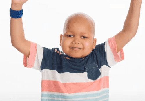 Boy with shaved head smiles and cheers.